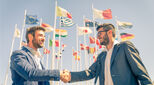 Two people shaking hands against background of flags